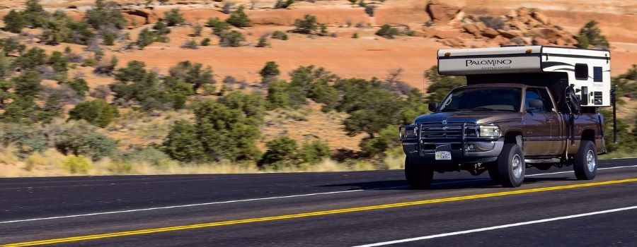 A truck with a camper driving on the road.
